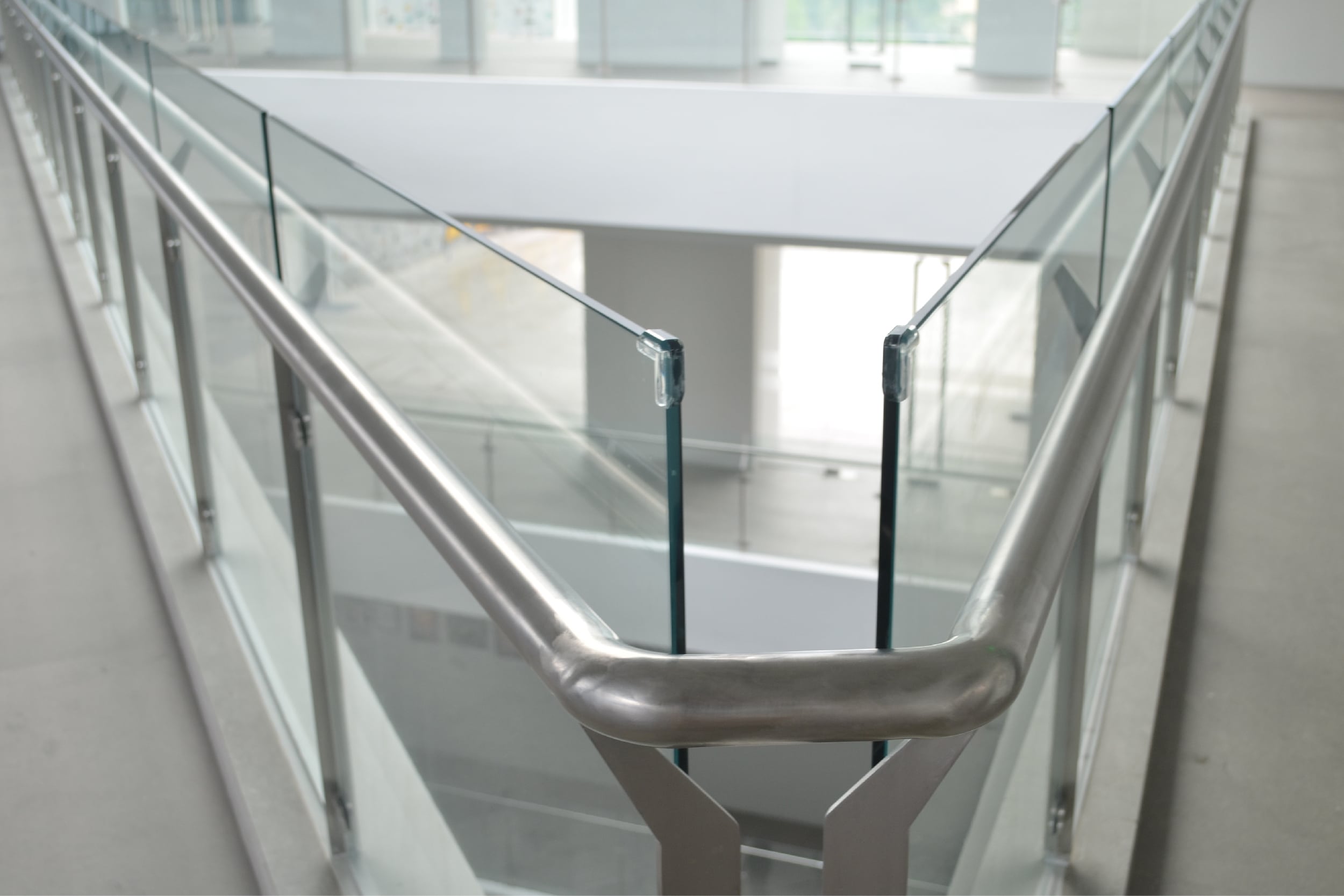 Post-and-clamp glass railing with stainless handrail delivers clear sightlines along a mezzanine edge.